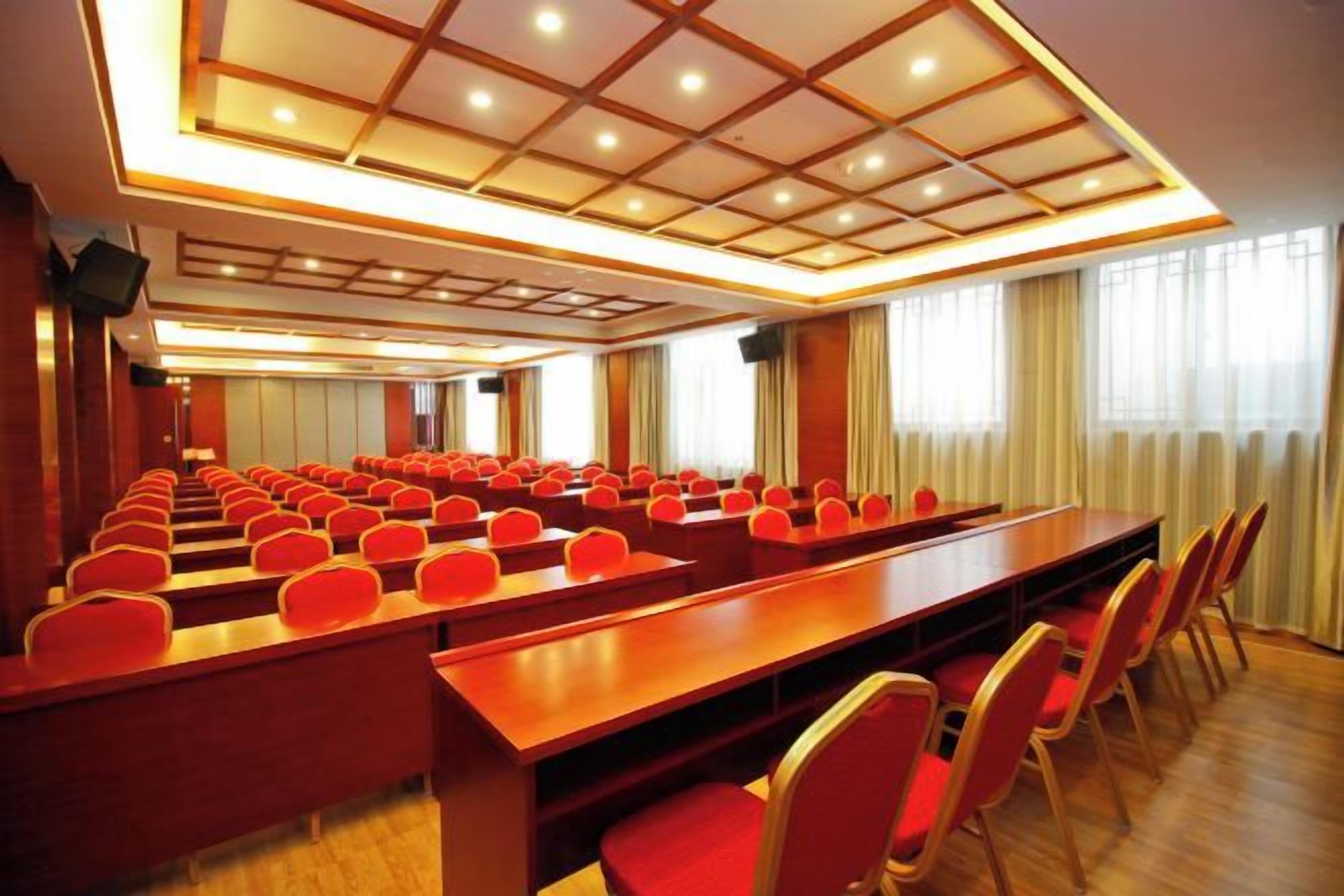 A conference room with rows of red chairs and a long table, equipped with a ceiling light fixture.