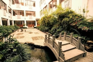 Un patio con un puente, plantas en macetas y una pequeña fuente.