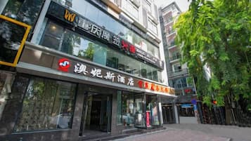 A building with a storefront featuring signage in a foreign language, a visible entrance, and a tree-lined street.