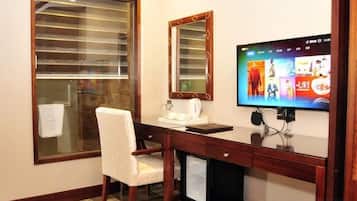 A hotel room with a desk, chair, television, and a large window with blinds.