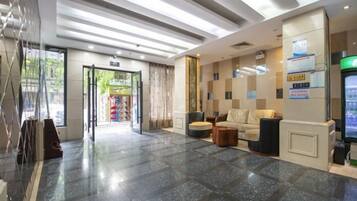 A hotel lobby with a reception desk, seating area, and a glass door entrance.