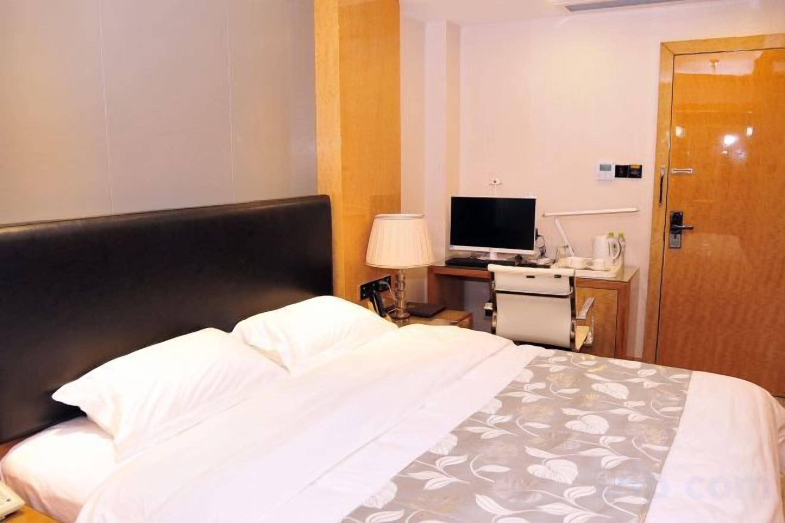 Une chambre d’hôtel avec un lit, un bureau avec un ordinateur, une télévision et une porte.