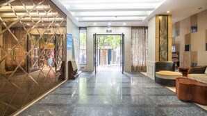 Ένα ξενοδοχειακό λόμπι με μαρμάρινο δάπεδο, έναν πάγκο υποδοχής και θέα προς το εξωτερικό.