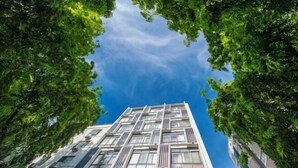 Ένα σύγχρονο κτίριο με μια σειρά από παράθυρα και μπαλκόνια, το οποίο περιβάλλεται από καταπράσινα δέντρα.