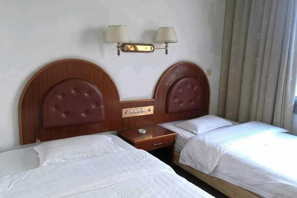 A hotel room with two beds, a nightstand, and a wall-mounted lamp.