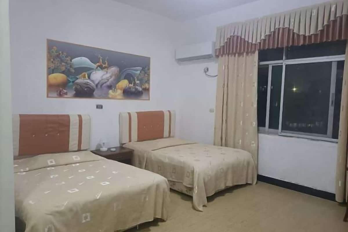 A hotel room with two beds, a painting on the wall, an air conditioning unit, and a window with curtains.