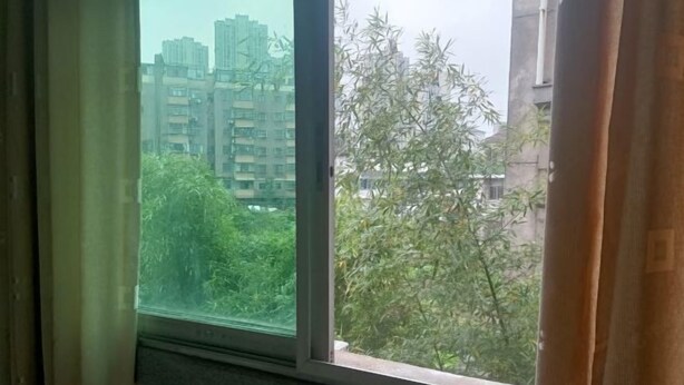 A window with a view of a cityscape and greenery. - Fuyang Station Front Hotel (Yiyang)