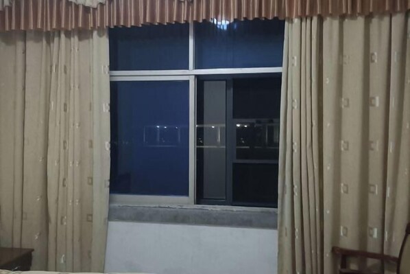 Una habitación con un ventanal grande, cortinas, una cama y una silla.