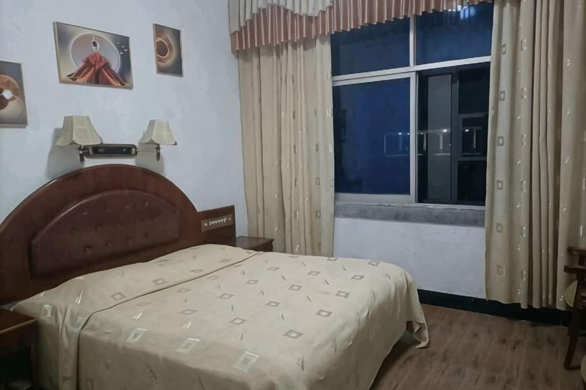 A bedroom with a bed, a nightstand, a window with curtains, and wall decorations.
