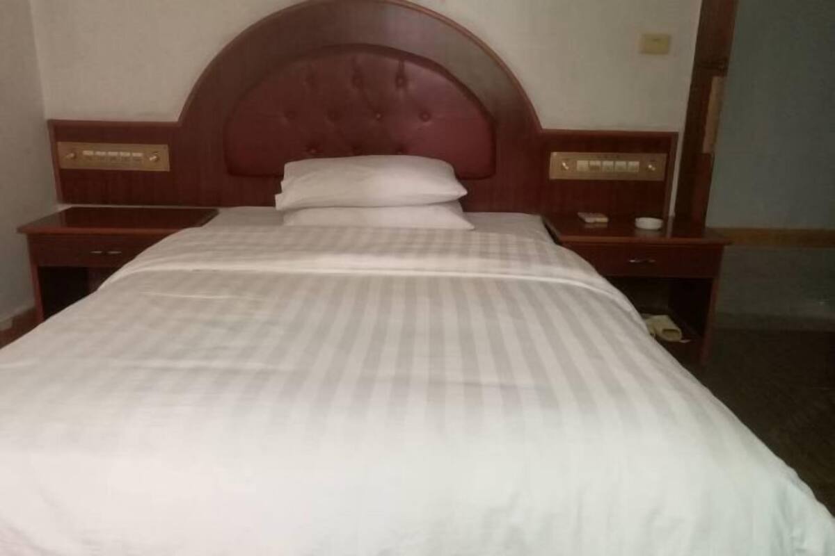 A hotel room with a large bed, wooden headboard, nightstands, and a mirror.