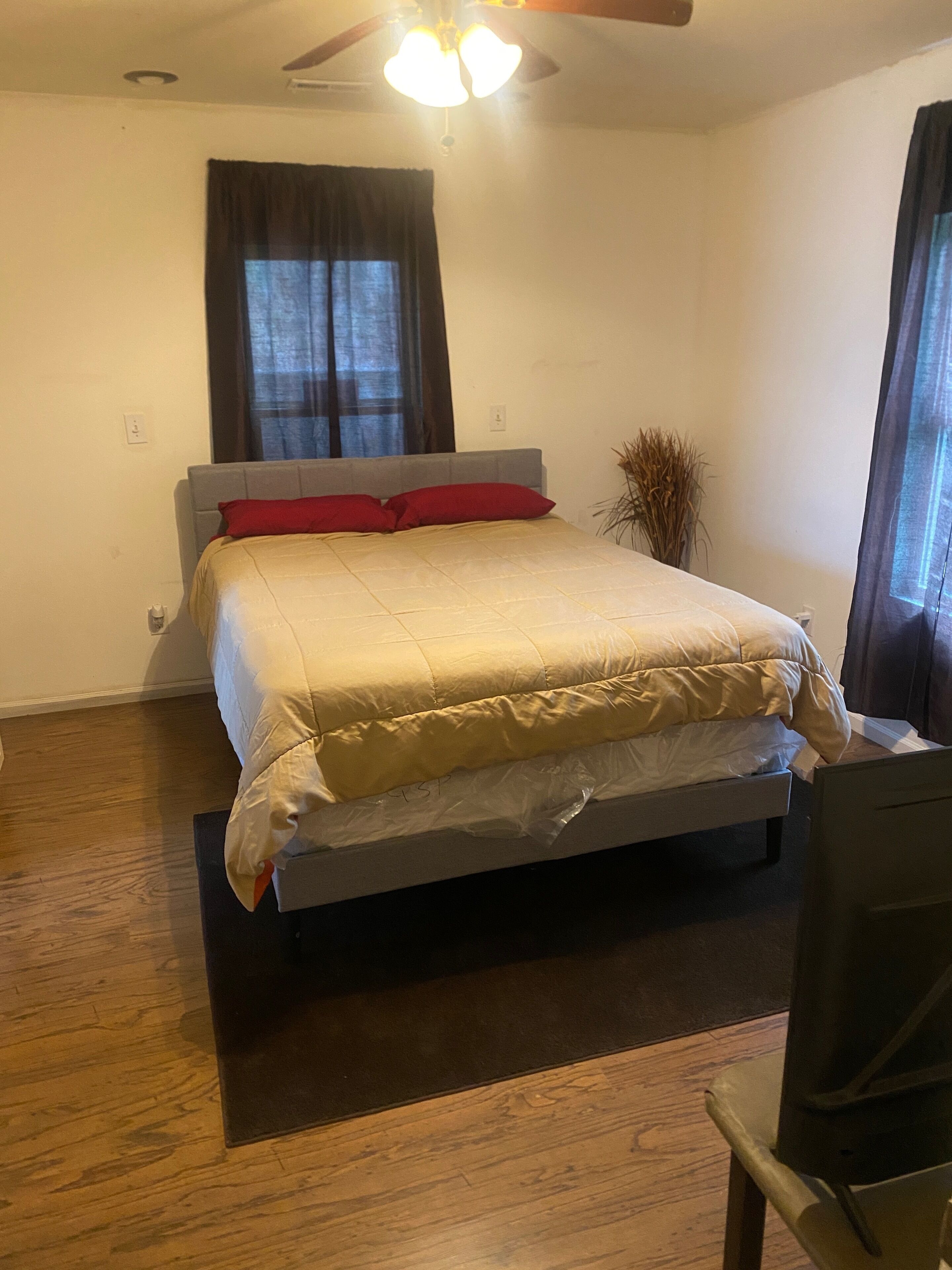 Een slaapkamer met een bed, een plafondventilator, een raam met gordijnen en een plant.