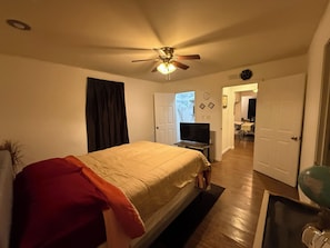 Ein Schlafzimmer mit einem Bett, einem Deckenventilator, einem Fernseher und einer Tür zu einem anderen Raum.
