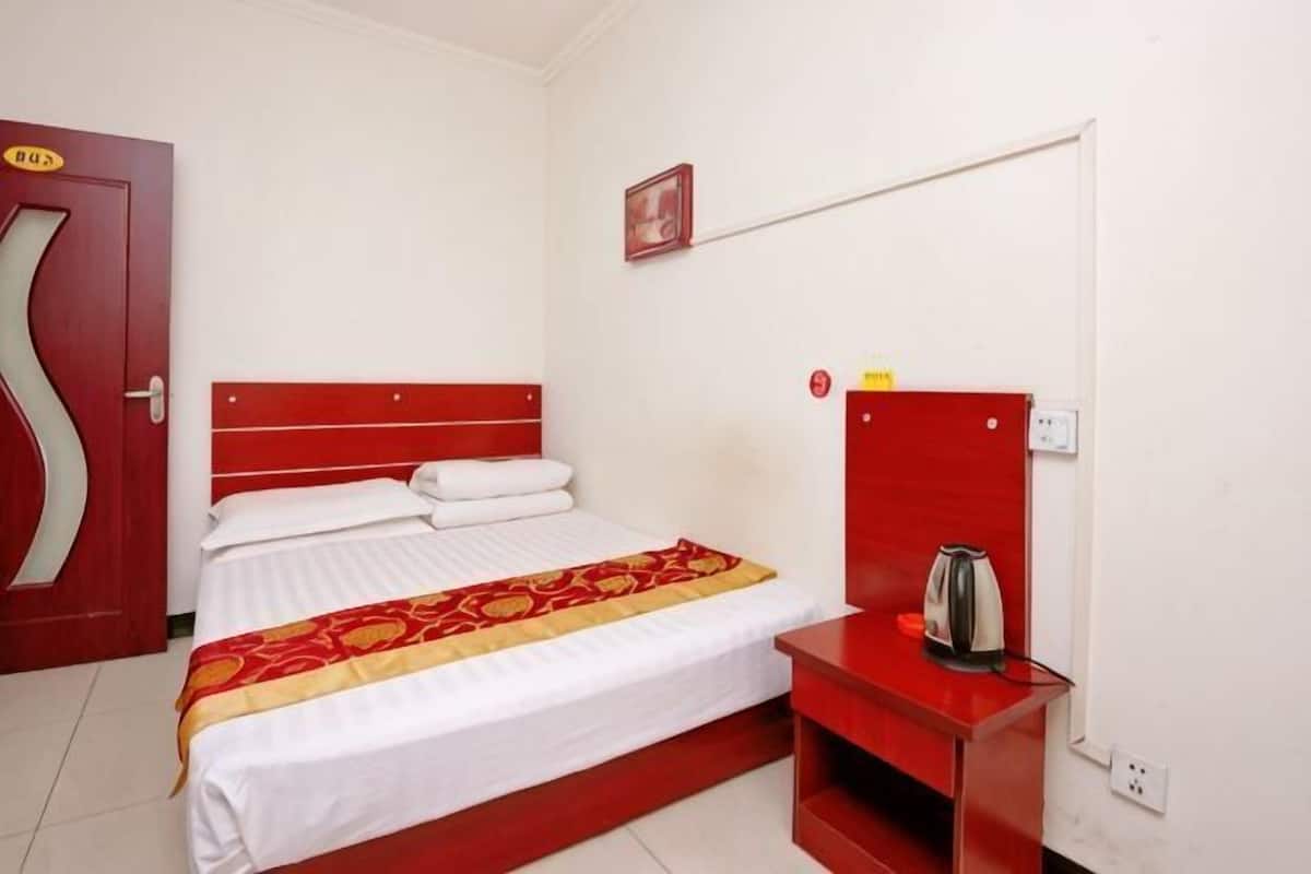 Hotelkamer met een bed, een rode nachtkastje met een waterkoker, een rode muur en een deur met een ruit.