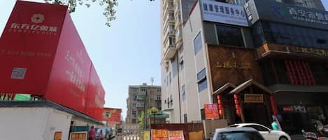 A street view with a red building on the left, a white car parked in front, and a tall building with signage on the right.