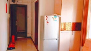A narrow hallway with a refrigerator and a cabinet, a door leading to another room, and a bed with a blanket. - Sunshine Hotel Xijing Hospital (Xi'an)