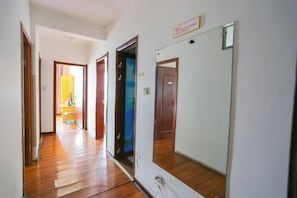 A hallway with wooden flooring, a mirror, and a door leading to another room.