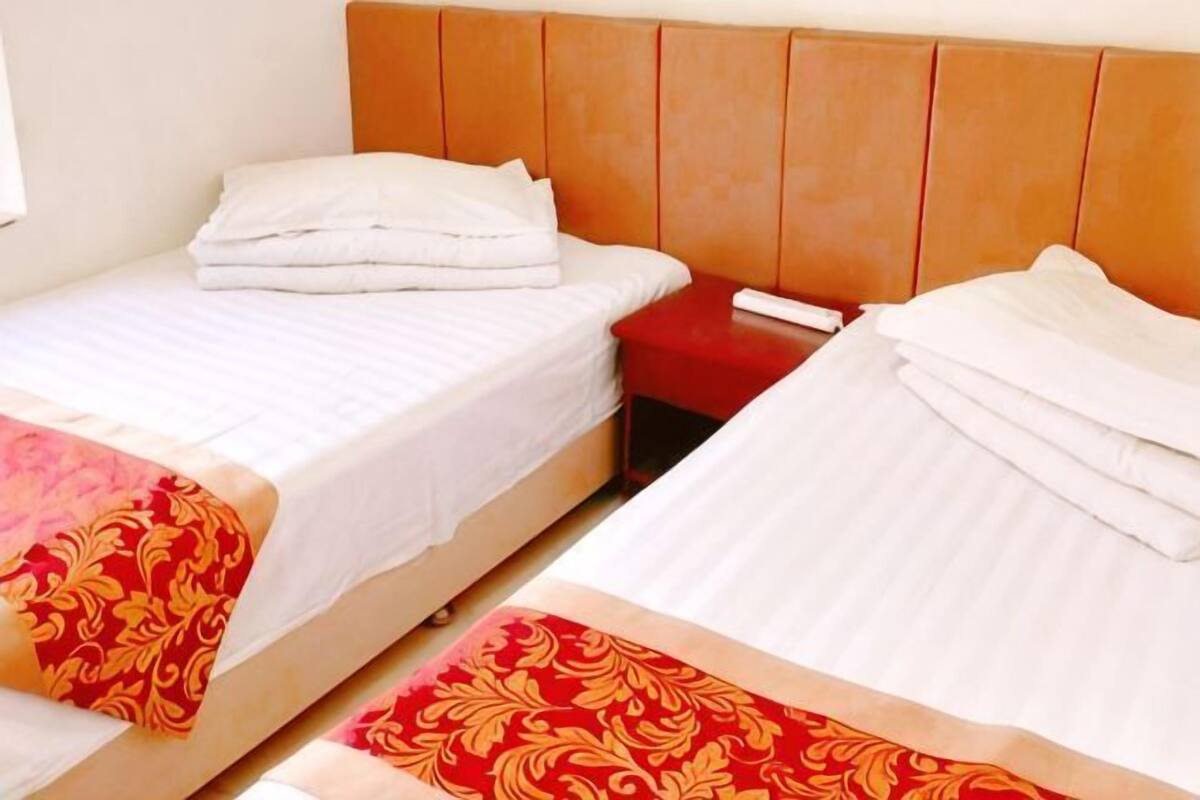 Twee eenpersoonsbedden met houten hoofdborden, witte beddengoed en rode decoratieve kussens.