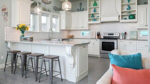 A kitchen with white cabinetry, a central island with stools, and a built-in oven. - Hot Tub & Direct Beach Access: Walk, Drive or Cart (Bolivar Peninsula)