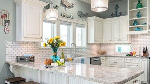 A kitchen with a large island, white cabinetry, and a tiled backsplash. - Hot Tub & Direct Beach Access: Walk, Drive or Cart (Bolivar Peninsula)