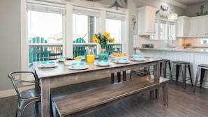 A kitchen with a long dining table, white cabinets, and a view of a blue deck. - Hot Tub & Direct Beach Access: Walk, Drive or Cart (Bolivar Peninsula)
