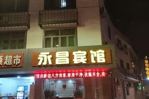 A hotel with a signboard displaying its name and a red neon sign indicating services.