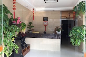 A reception area with a counter, potted plants, and a wall clock. - Yongchang Hotel (Ningbo)