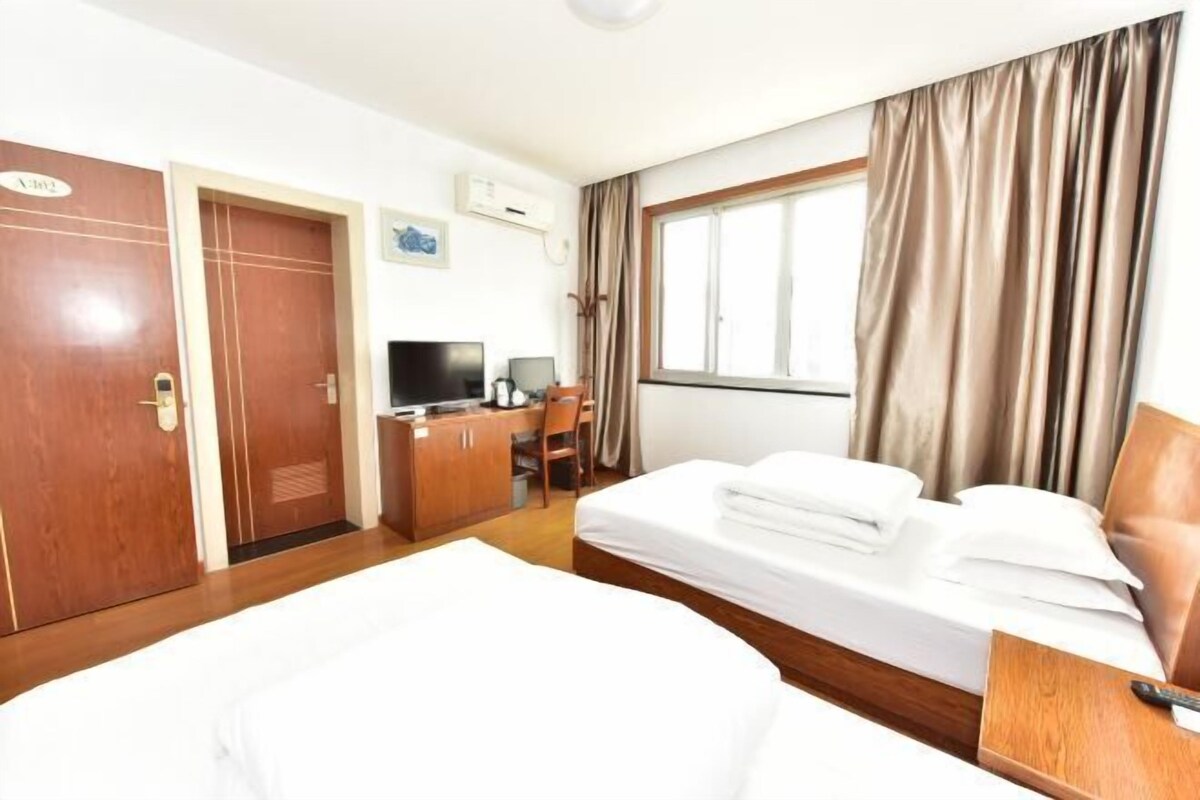 A hotel room with a large bed, a desk with a computer, a TV, and a window with curtains.