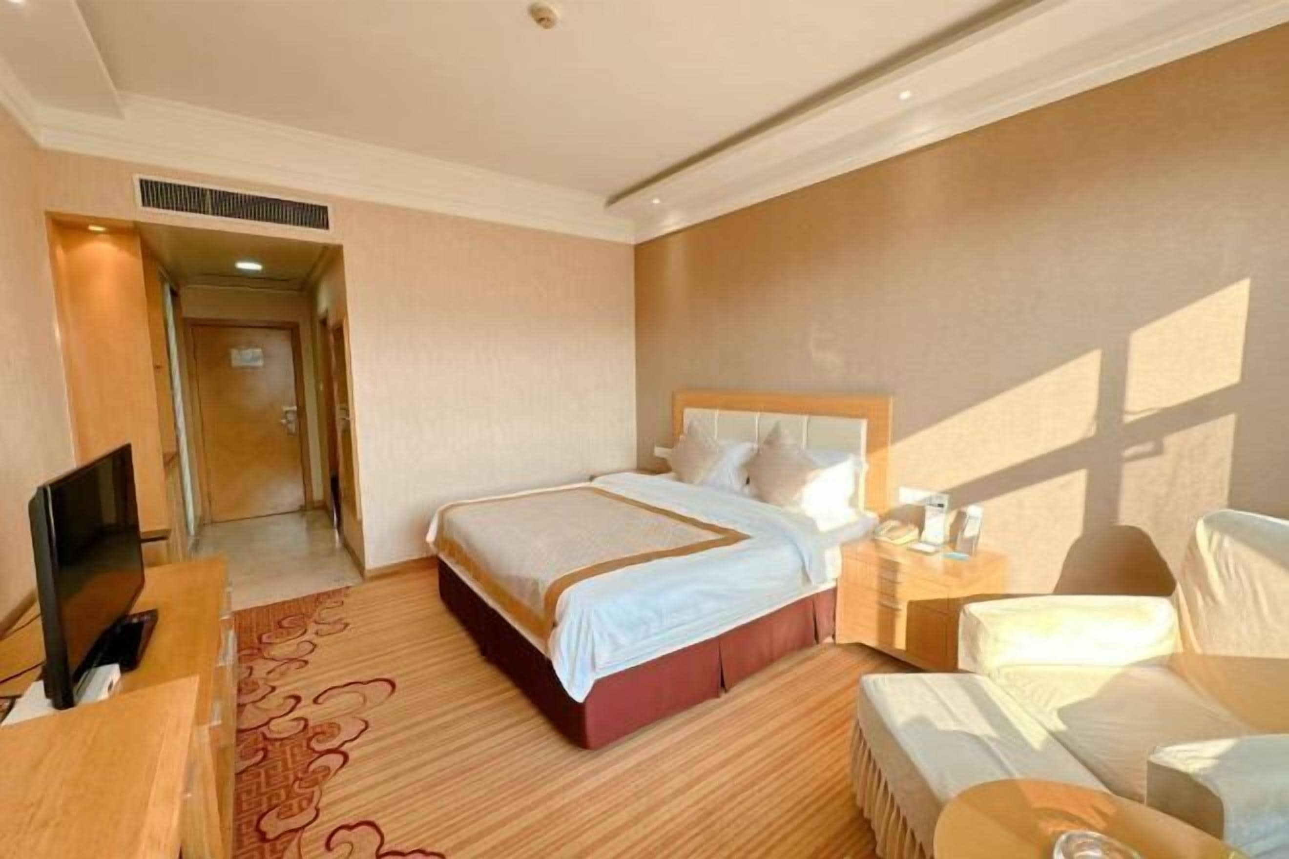 A hotel room with a bed, a desk with a TV, a chair, and a bedside table.