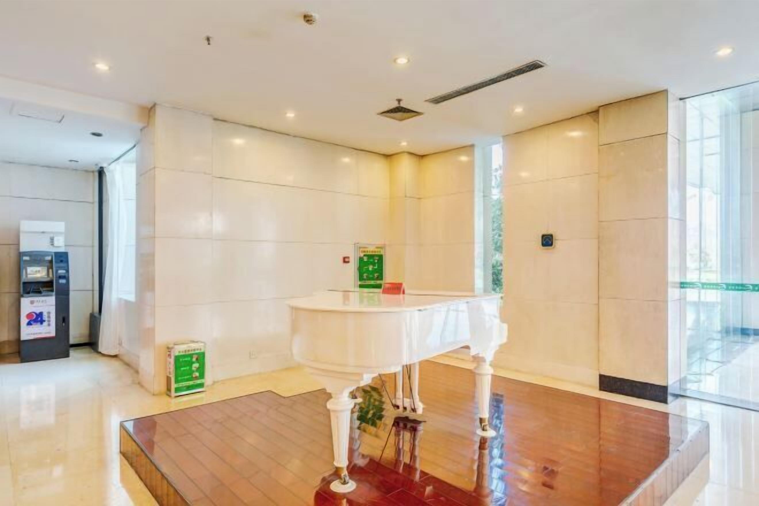 Um lobby moderno com piso de mármore, balcão de recepção e caixa eletrônico disponível 24 horas.