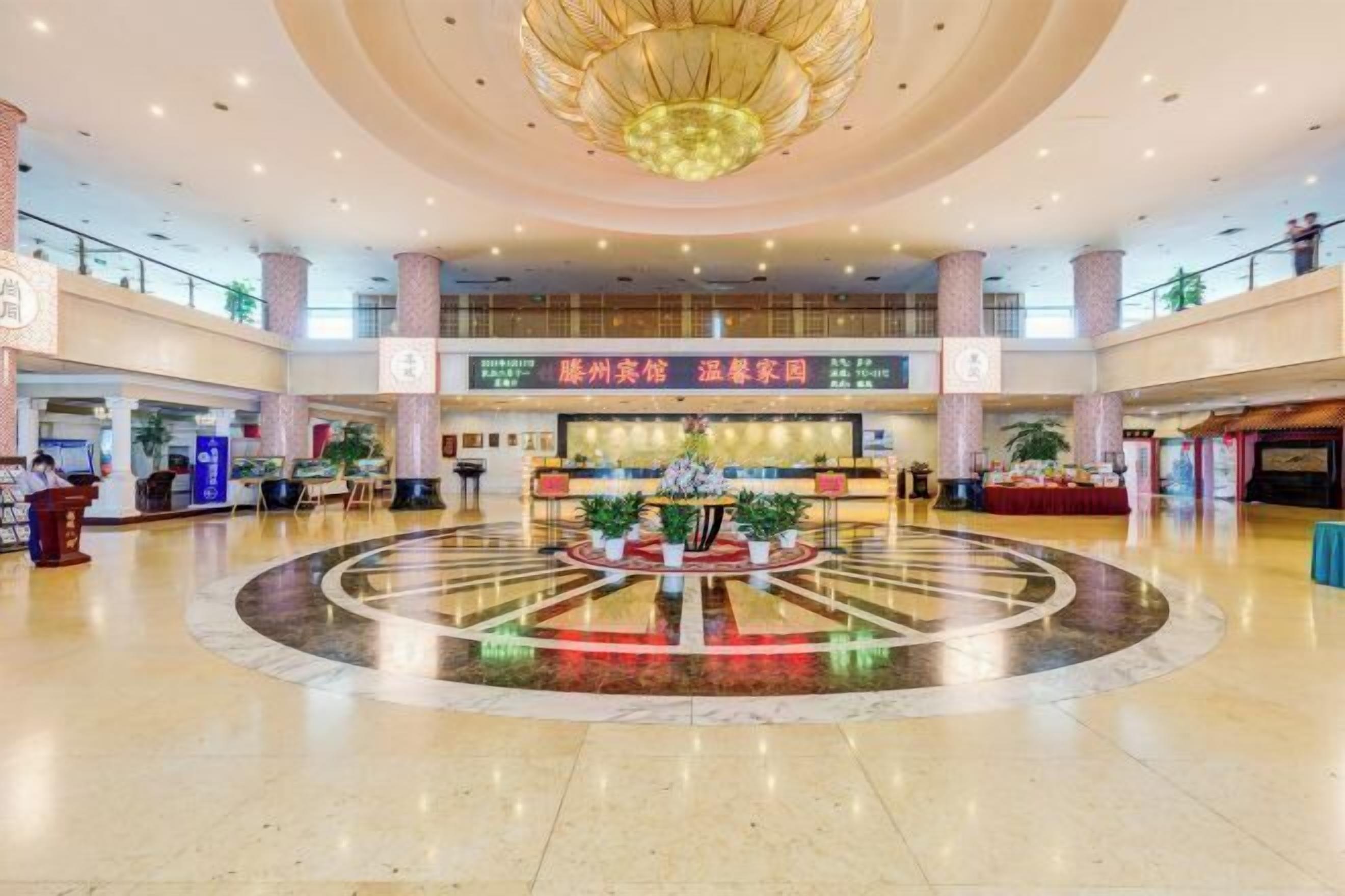 Un vestíbulo amplio con una zona circular central que presenta una recepción, plantas en macetas y un candelabro.