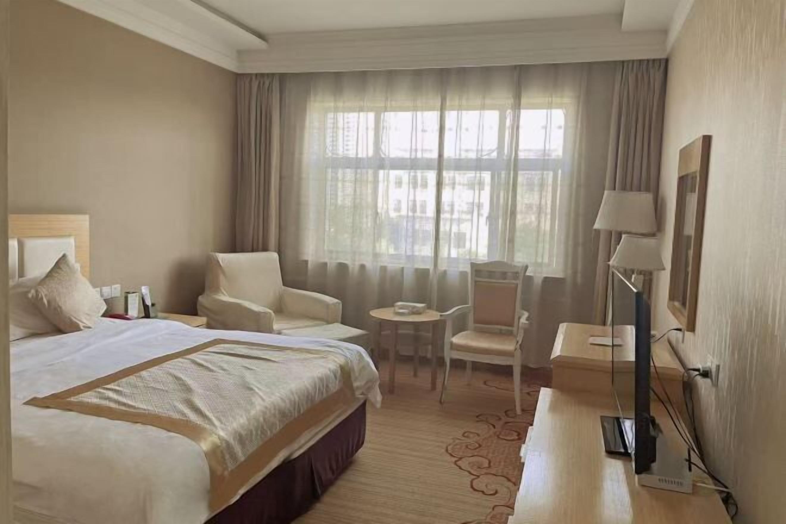 Una camera d'albergo con un letto grande, una scrivania, una sedia, un tavolino e una televisione.