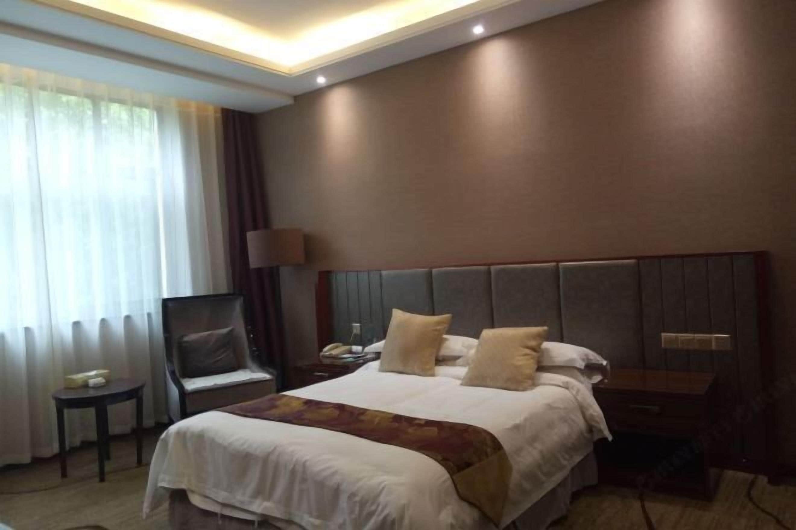 A hotel room with a large bed, a bedside table, a chair, and a nightstand.
