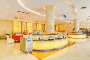 Vestíbulo de hotel con zona de buffet central, mostrador de recepción y área de descanso con sillas.