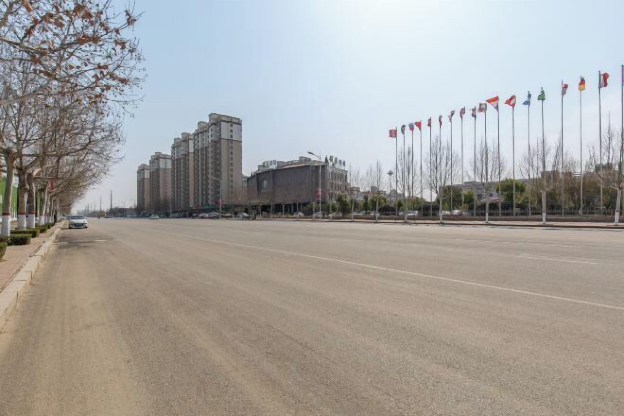 Una carretera amplia y vacía con edificios altos y asta de banderas a la derecha.