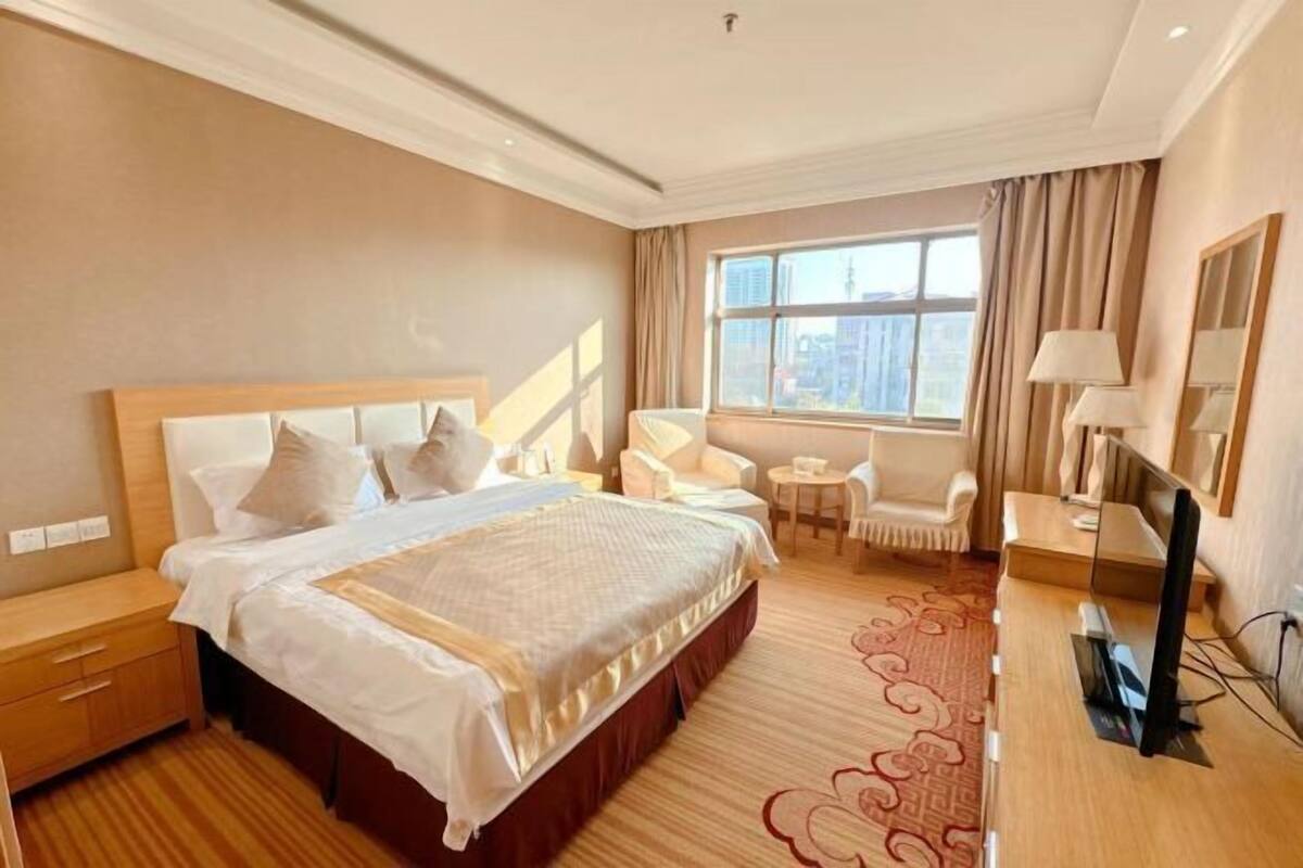 Ein Hotelzimmer mit einem großen Bett, einem Schreibtisch, einem Sessel, einem kleinen Tisch und einem Fernseher.