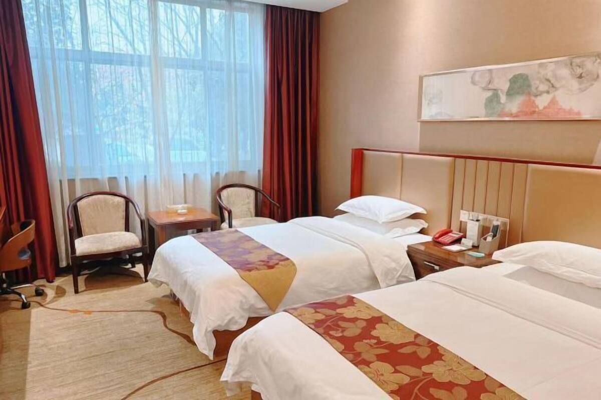 Ein Hotelzimmer mit zwei Betten, einem Schreibtisch, einem Stuhl und einem fenster mit Vorhängen.