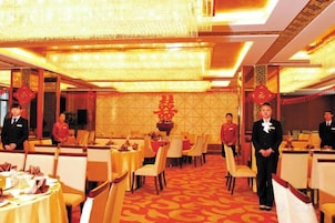 A banquet hall with round tables, waitstaff in uniform, and a patterned carpet.