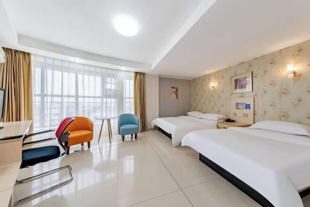 A hotel room with two beds, a desk, a chair, and a large window with curtains.