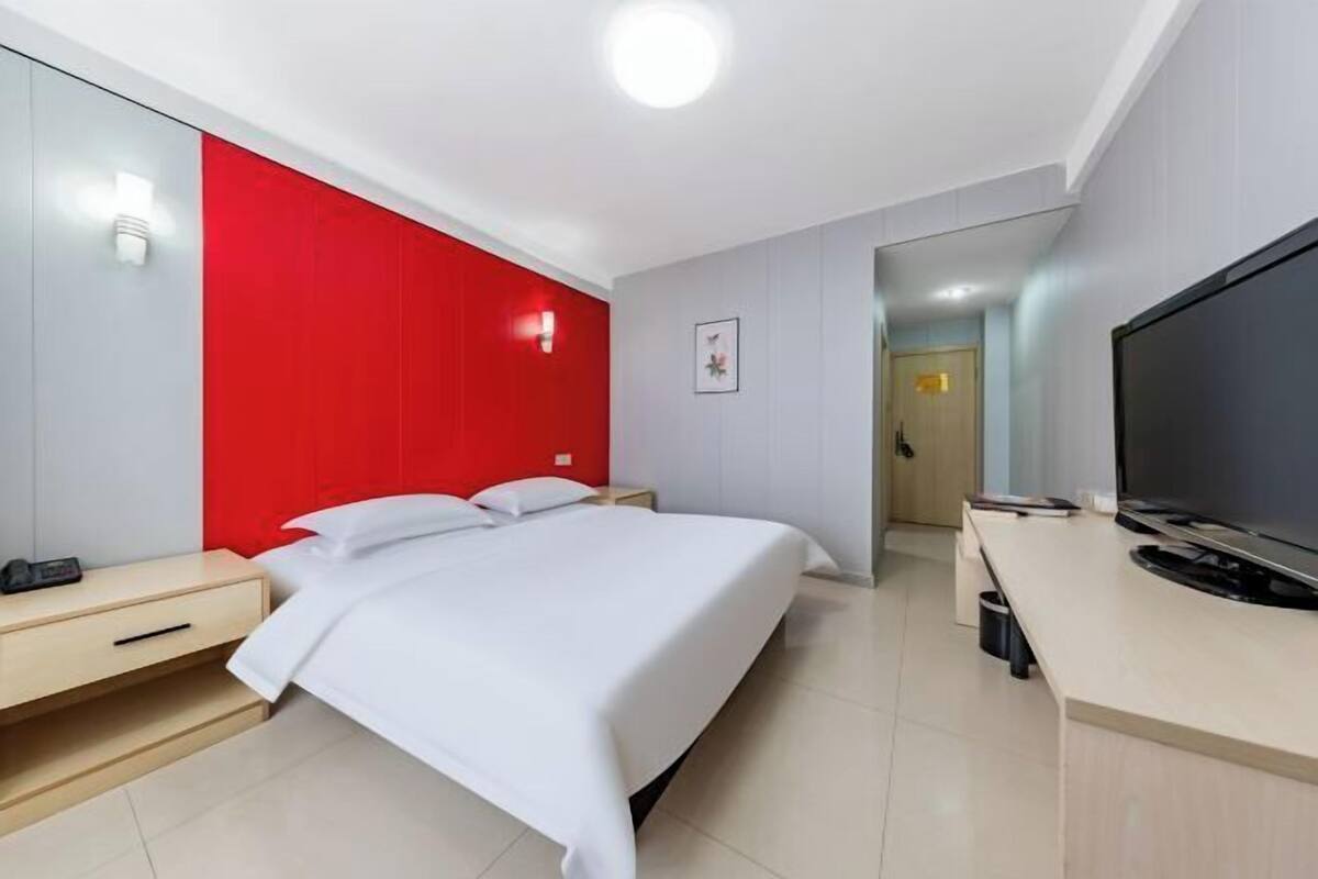 A hotel room with a bed, a desk with a television, and a mirror.