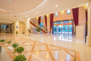 Un amplio vestíbulo con suelo de mármol, una escalera y una mesa de recepción.