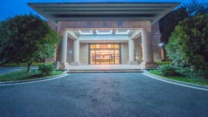 A modern building with a large entrance, a covered walkway, and a well-maintained garden area. - Qing He Hotel (Hangzhou)