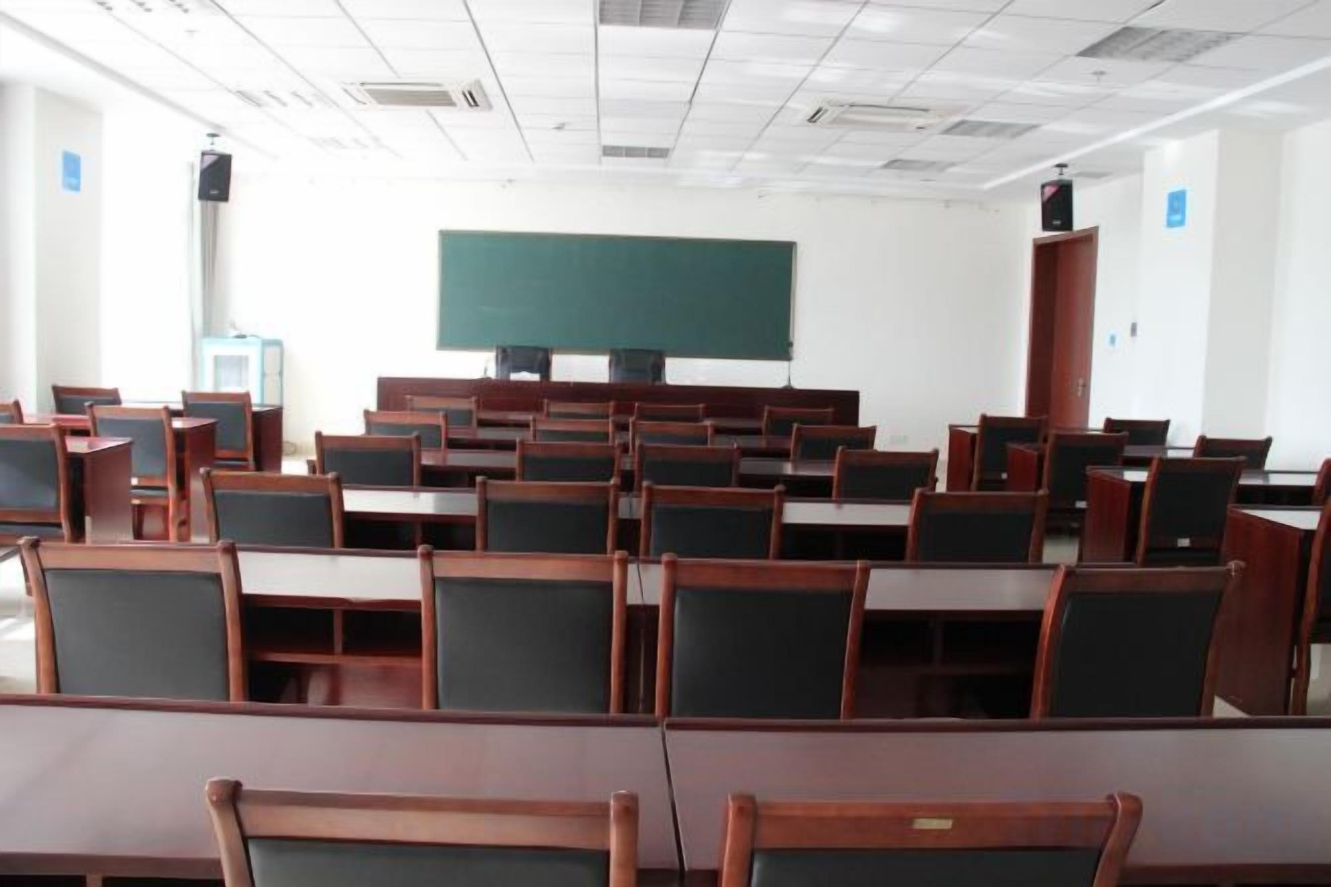 Un aula con filas de escritorios y sillas, una pizarra y un altavoz.