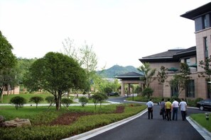 A pathway leading to a building with a covered entrance, surrounded by greenery and a mountain in the background. - Qing He Hotel (Hangzhou)