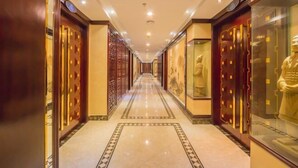A corridor with ornate doors and glass display cases, leading to a long hallway with a tiled floor and recessed lighting. - Qing He Hotel (Hangzhou)