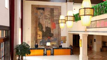 Un vestíbulo de hotel con mostrador de recepción, un mural grande y lámparas colgantes.