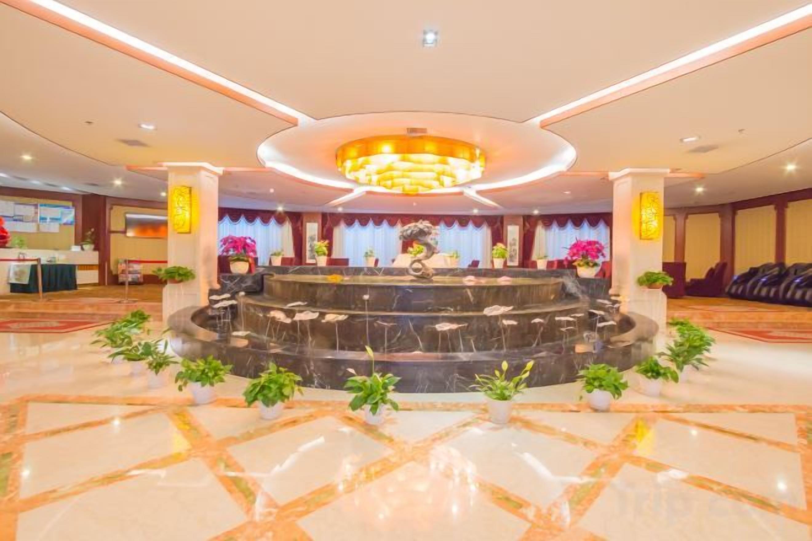 A hotel lobby with a central fountain, marble flooring, and a reception desk.