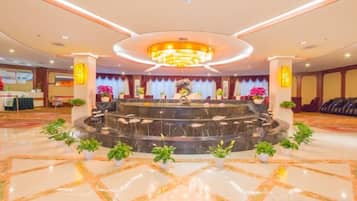 A hotel lobby with a central fountain, marble flooring, and a reception desk.