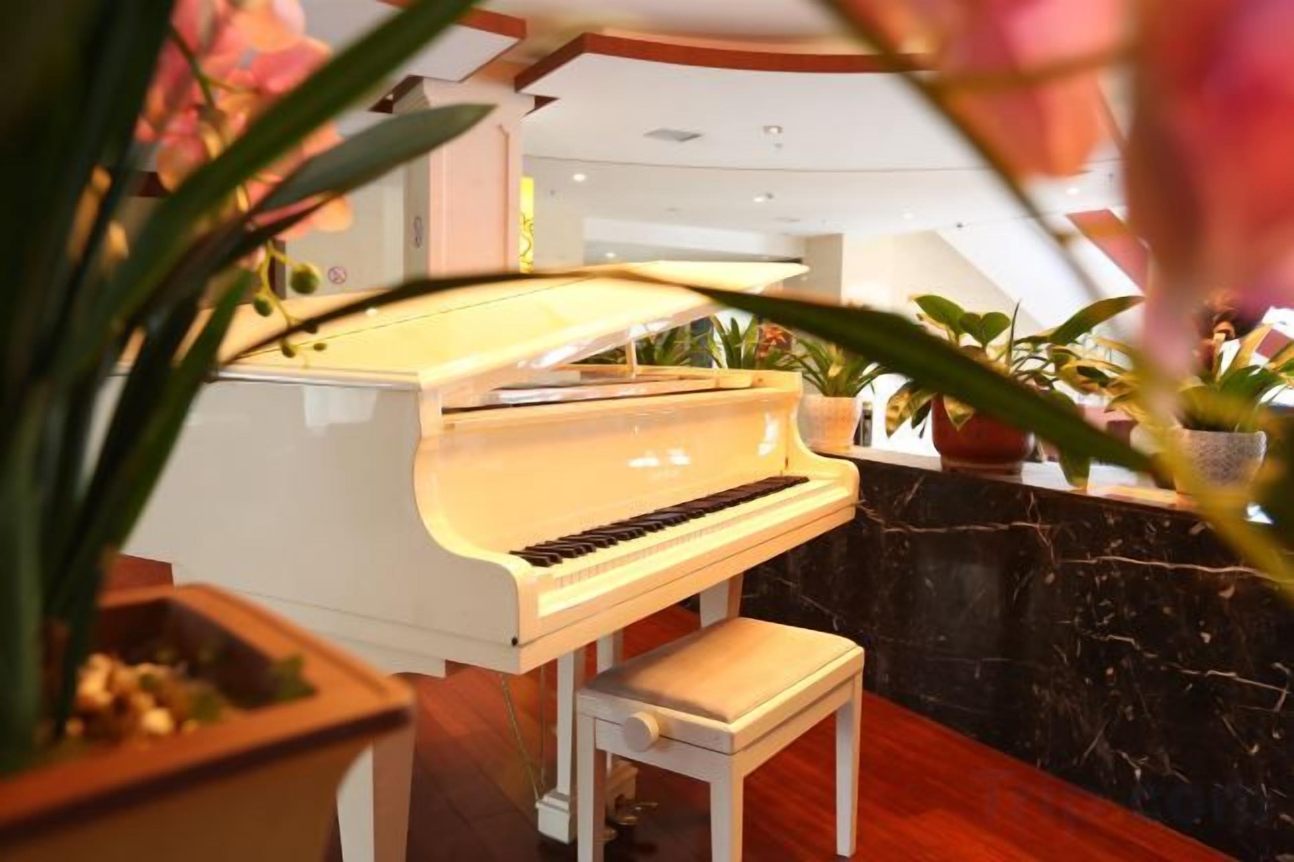 A grand piano in a well-lit room with a marble floor and potted plants.
