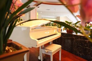 A grand piano in a well-lit room with a marble floor and potted plants. - Qing He Hotel (Hangzhou)