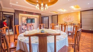 A dining area with round tables, wooden chairs, and a central chandelier. - Qing He Hotel (Hangzhou)